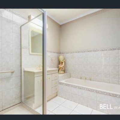 Bathroom with tiled walls, glass shower enclosure, white vanity, and bathtub.