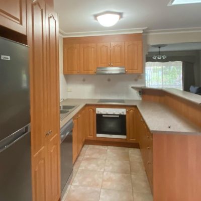 Kitchen with wooden cabinets, stainless steel appliances, tiled floor, and overhead lighting.