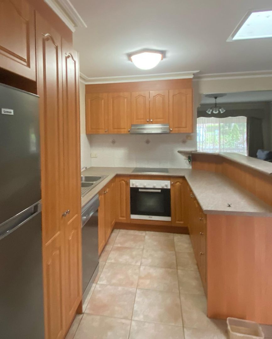 Kitchen with wooden cabinets, stainless steel appliances, tiled floor, and overhead lighting.