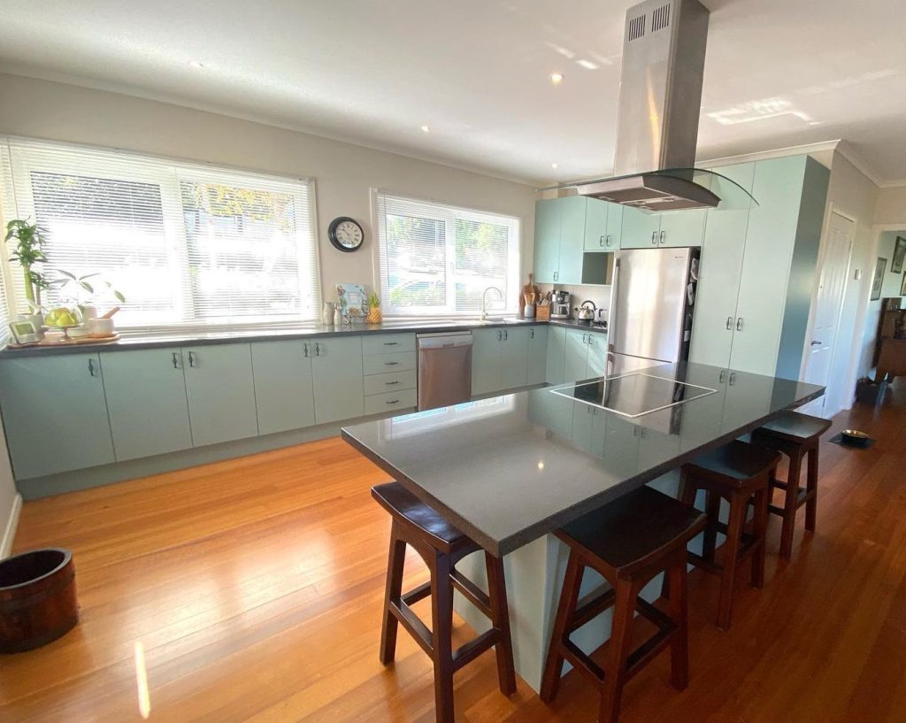 Modern kitchen with light blue cabinets, large island with dark countertop, and stainless steel appliances.