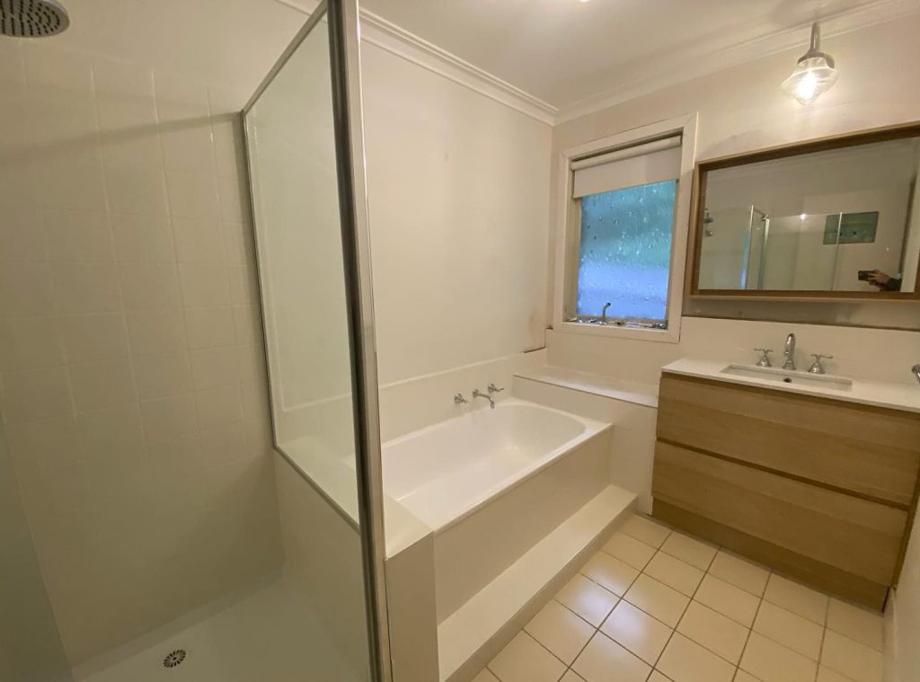 Bathroom with glass-enclosed shower, white bathtub, wooden vanity, and frosted window.