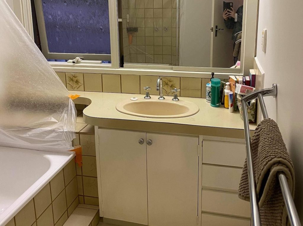 Bathroom with beige countertop and sink, partially covered bathtub, and personal hygiene items.