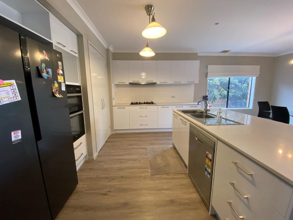 Modern kitchen featuring resurfaced white cabinets, black refrigerator, double oven, gas stove, sink on an island, and dishwasher.