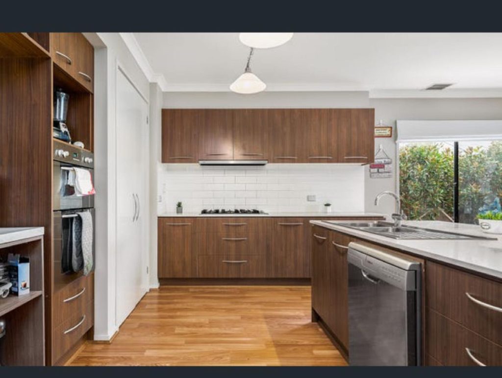 Modern kitchen with wooden cabinets, built-in oven, gas stovetop, white subway tile backsplash, double sink, dishwasher, and polished wood flooring.