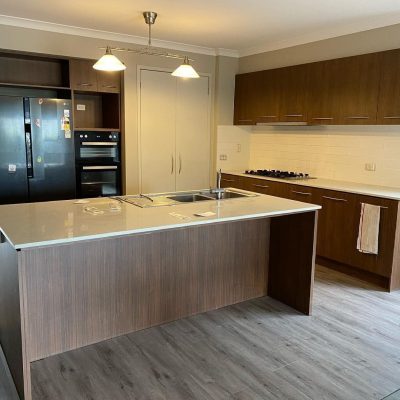 Modern kitchen with wooden cabinets, central island with sink, double-door refrigerator, built-in oven, and stovetop.