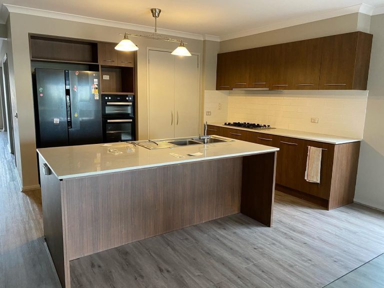 Modern kitchen with wooden cabinets, central island with sink, double-door refrigerator, built-in oven, and stovetop.