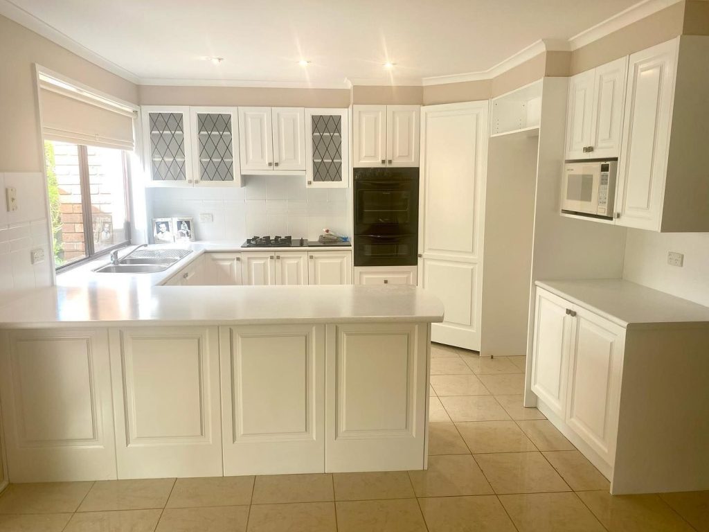 A modern kitchen with white resurfaced cabinetry, built-in appliances, and a central island.