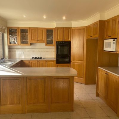 Kitchen with wooden cabinets, double sink under window, built-in microwave and oven, gas stovetop, and tiled floor.