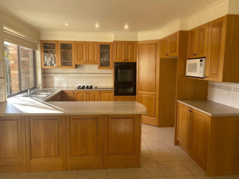 Kitchen with wooden cabinets, double sink under window, built-in microwave and oven, gas stovetop, and tiled floor.