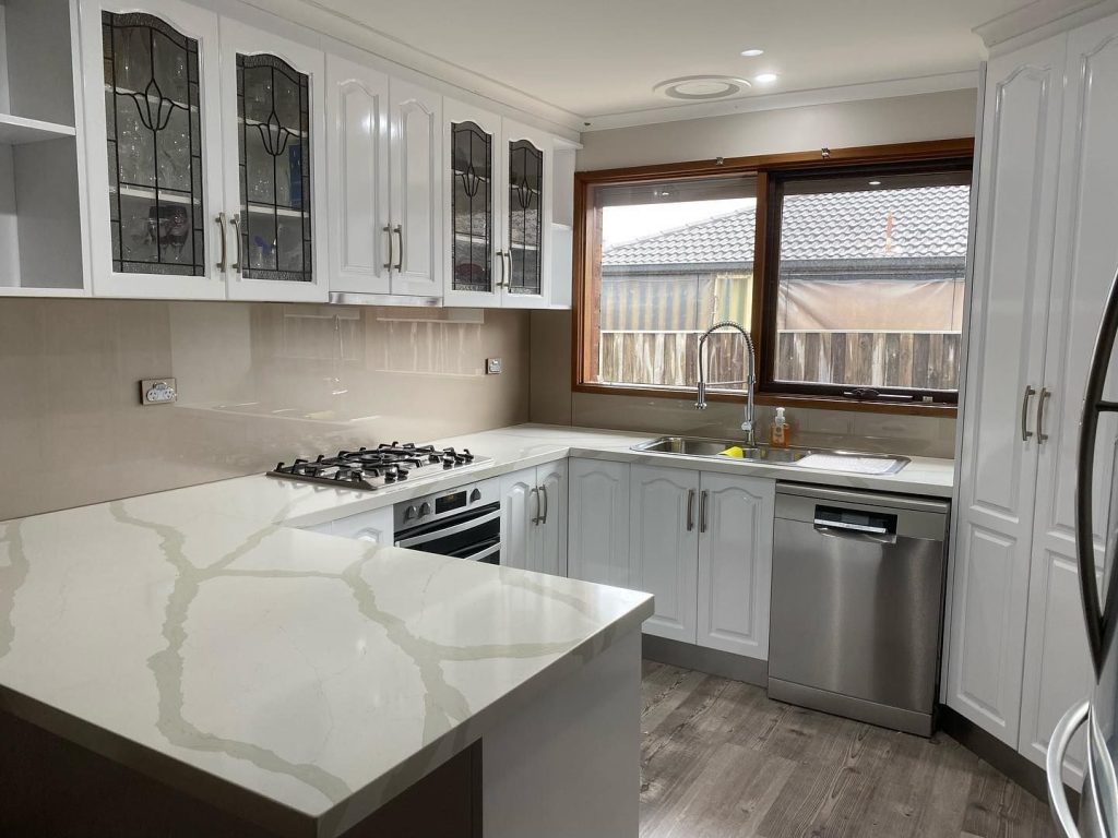 Modern kitchen featuring resurfaced white cabinets, stainless steel gas stove, oven, dishwasher, double sink under a large window.