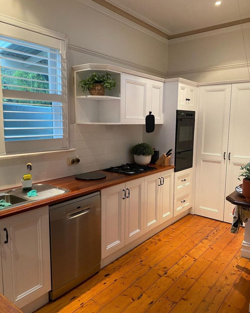 Modern kitchen with white cabinets, wooden countertops, gas stove, oven, dishwasher, and potted plants.