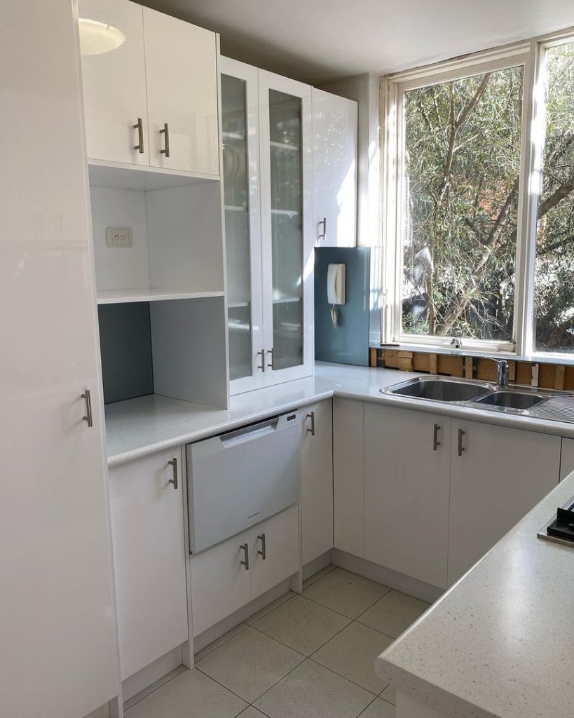 Modern kitchen with white cabinets, double sink, built-in dishwasher, and large window.