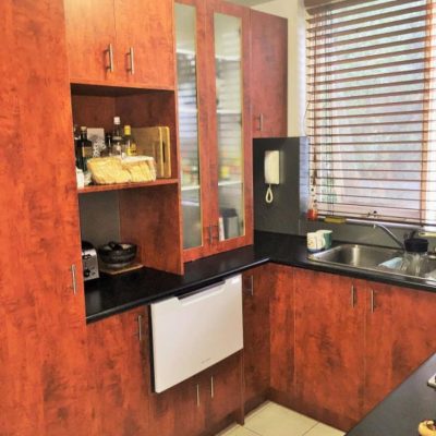 Kitchen corner with reddish-brown wooden cabinets, black countertop, integrated dishwasher, and double sink under a window with blinds.