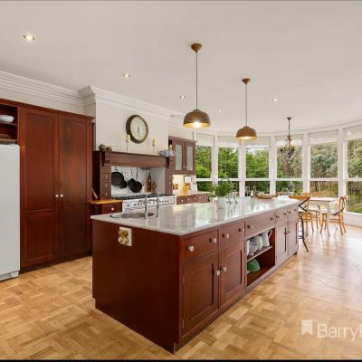 Large kitchen with wooden cabinets, marble countertops, central island, pendant lights, and dining area near large windows.