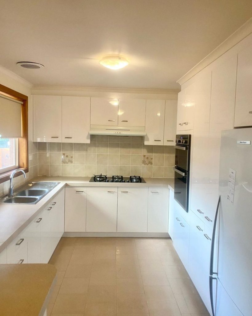 Modern kitchen with white cabinets, gas stovetop, built-in oven, double sink, and light beige tiled backsplash.