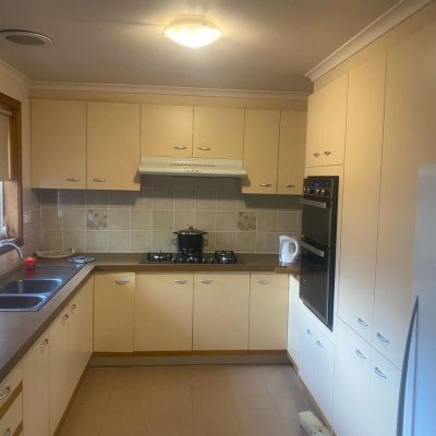 Kitchen with beige cabinets, double sink, stovetop, oven, microwave, and tiled backsplash.