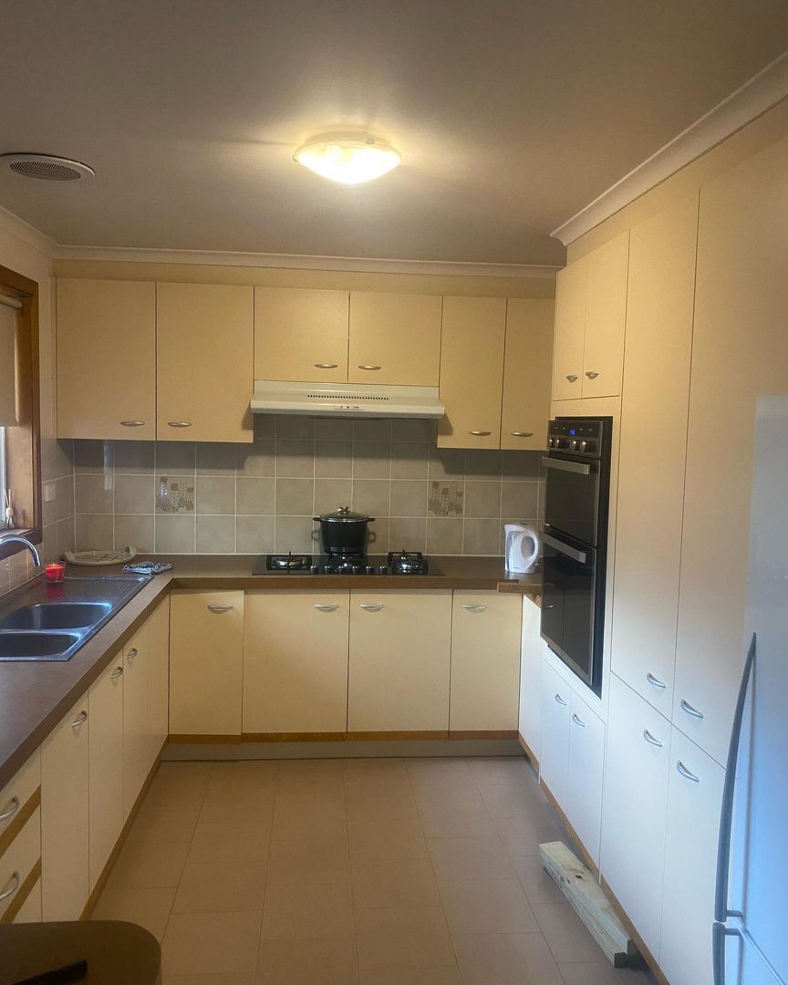 Kitchen with beige cabinets, double sink, stovetop, oven, microwave, and tiled backsplash.