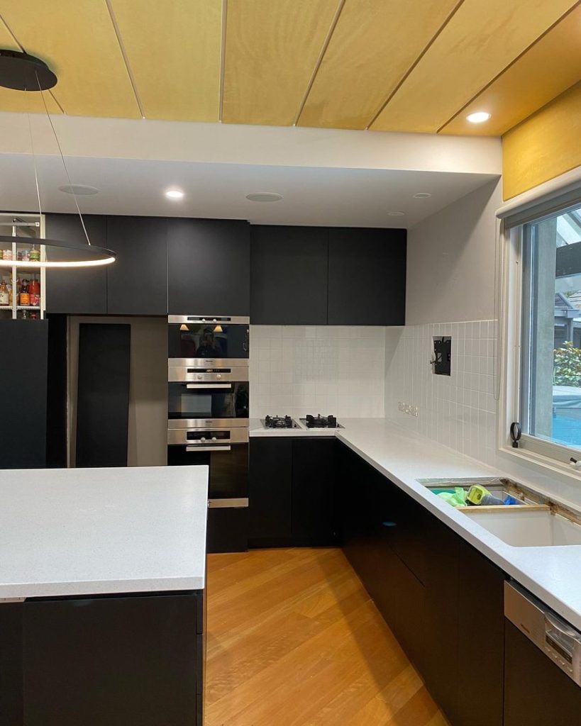 Modern kitchen with black cabinets, white countertops, built-in stainless steel appliances, gas stovetop, and wooden flooring.