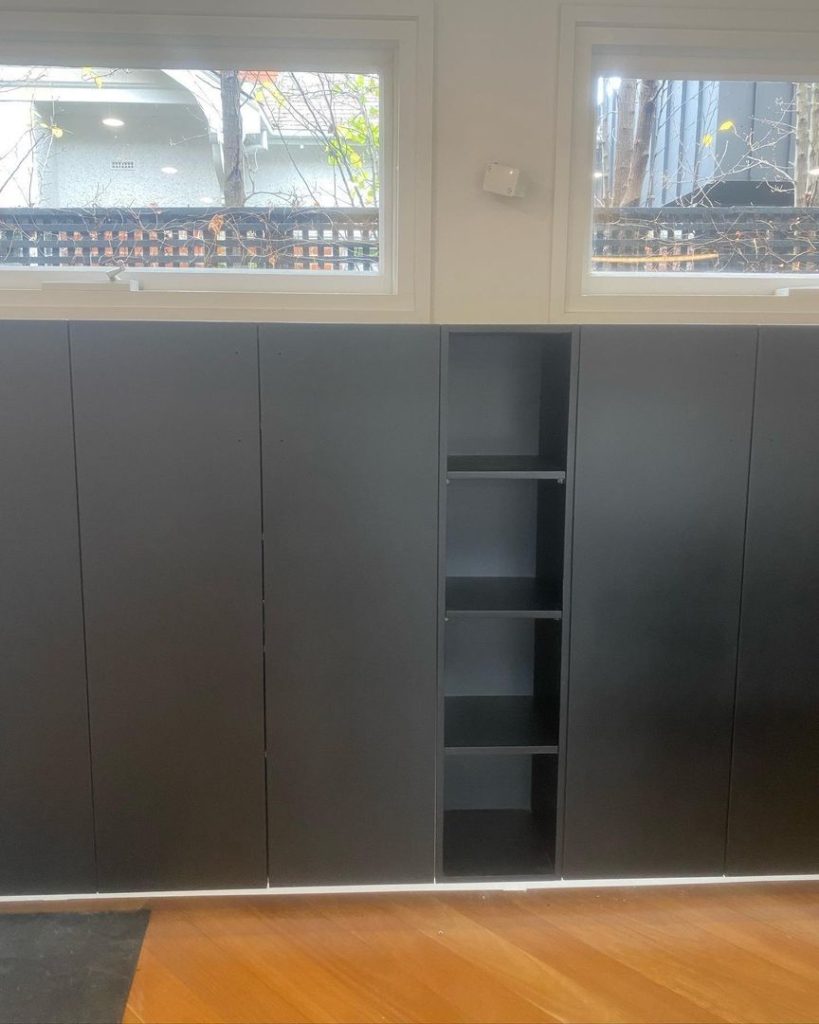 Black kitchen cabinets with open shelving under two windows in a modern kitchen.