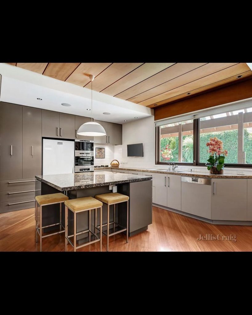 Modern kitchen featuring granite countertops, stainless steel appliances, grey cabinets, and large windows.