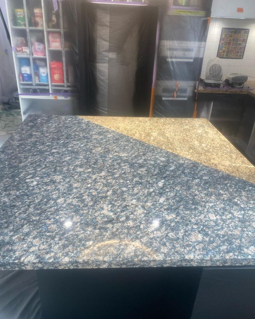 Granite kitchen countertop with surrounding shelves and covered cabinets during resurfacing work.