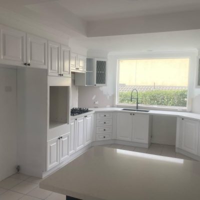 Modern white kitchen with resurfaced cabinets, large window, and built-in stovetop.