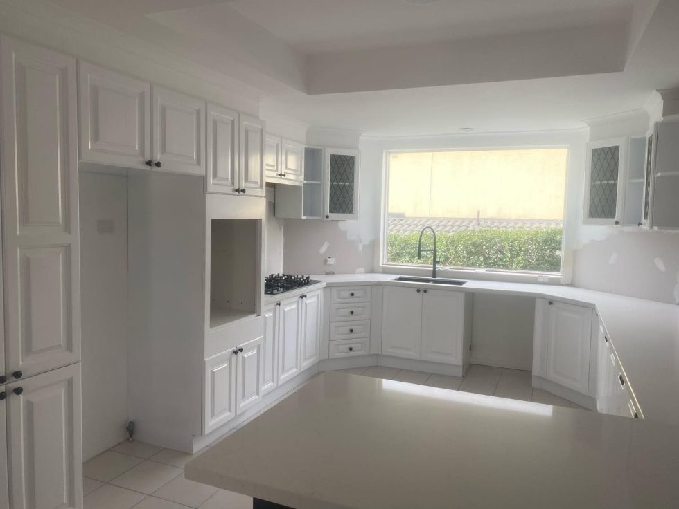 Modern white kitchen with resurfaced cabinets, large window, and built-in stovetop.