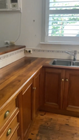 Kitchen featuring wooden countertops and cabinets, stainless steel sink, white tiled backsplash, window with shutters, and wall-mounted air conditioning unit.