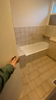 Person opening door to a partially renovated bathroom with beige tiles and white bathtub