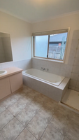 Image of an older bathroom with a bathtub under a window, a sink, and a vanity showing signs of wear.