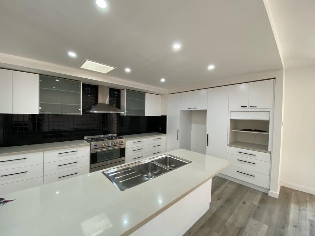 Renovated modern kitchen with white cabinets, central island, double sink, stainless steel appliances, and black tile backsplash.