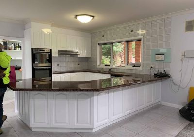 Modern kitchen with granite countertop island, white cabinets, stainless steel double oven, and large window.