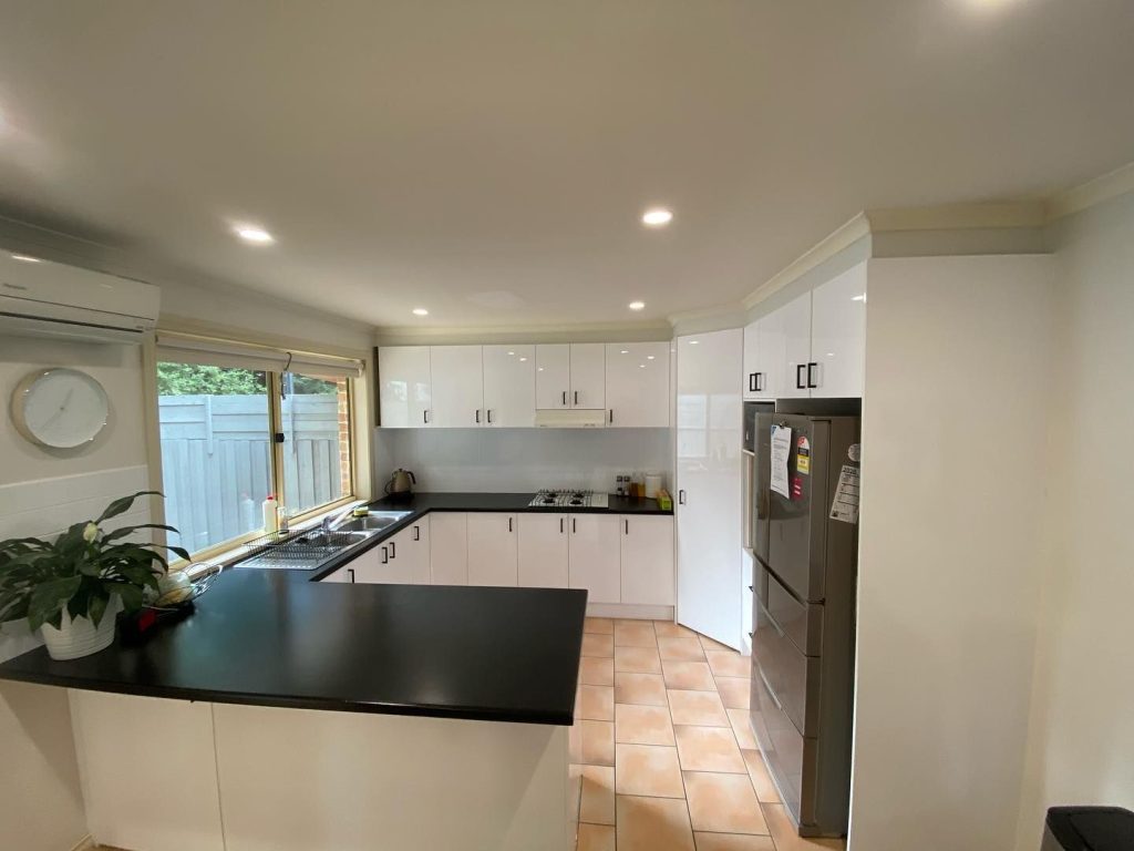 Modern kitchen featuring white cabinets, black countertops, stainless steel refrigerator, and large window.