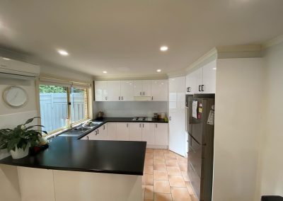 Modern kitchen featuring white cabinets, black countertops, stainless steel refrigerator, and large window.