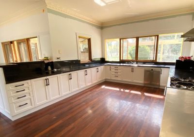 Renovated kitchen with white cabinets, black countertops, stainless steel appliances, hardwood flooring, and large windows.
