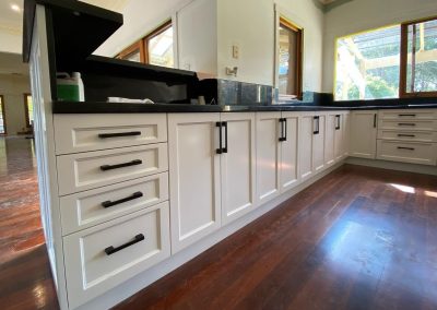 Renovated kitchen with white cabinets, black countertops, and wooden floors.