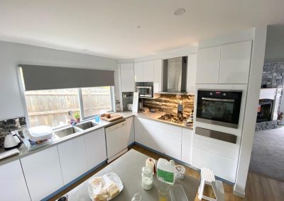Modern kitchen with white cabinets, stainless steel appliances, and rustic stone backsplash.