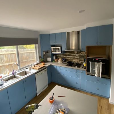 Modern kitchen with blue cabinets, stainless steel appliances, wooden flooring, and stone tile backsplash.