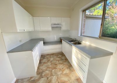 Modern kitchen with white cabinets, grey countertops, and large window.