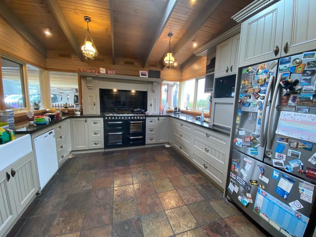 Rustic kitchen with wooden ceilings, cream cabinets, black stove, and slate tile flooring.