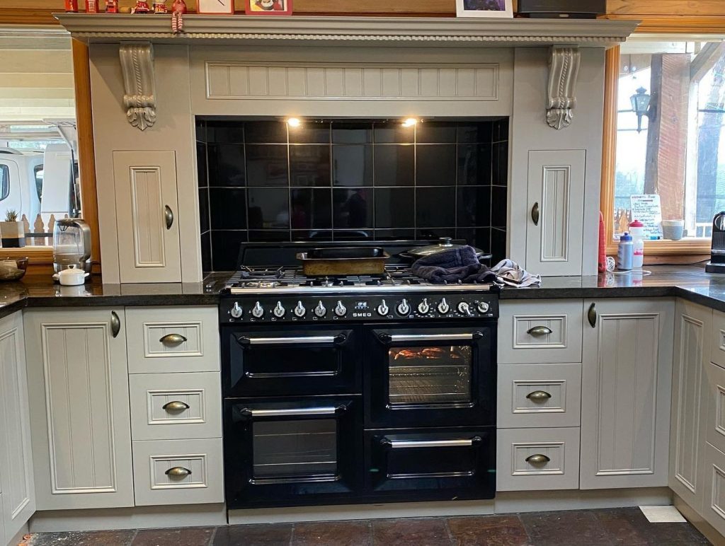 Renovated kitchen featuring a central black stove, white cabinetry, granite countertops, and decorative molding.