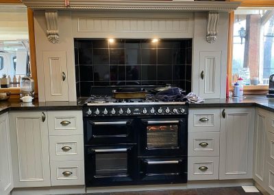 Renovated kitchen featuring a central black stove, white cabinetry, granite countertops, and decorative molding.