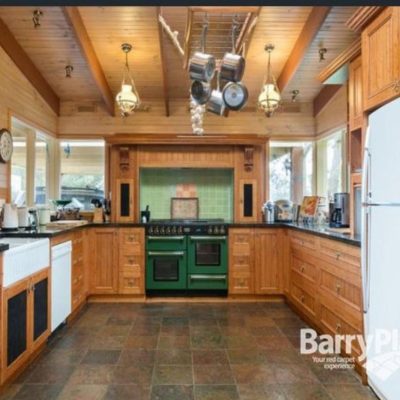 Renovated kitchen with wooden cabinets, green stove, farmhouse sink, and hanging pots.