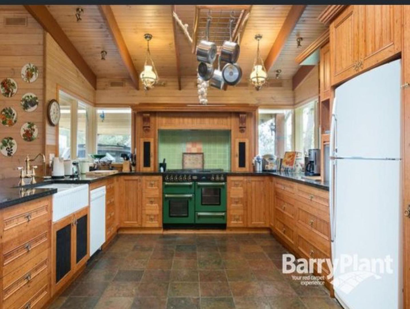 Renovated kitchen with wooden cabinets, green stove, farmhouse sink, and hanging pots.