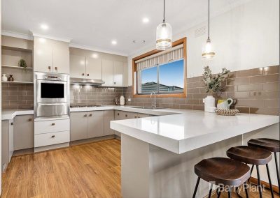 Modern kitchen with white quartz countertops, stainless steel appliances, light gray cabinets, wooden flooring, and decorative items.