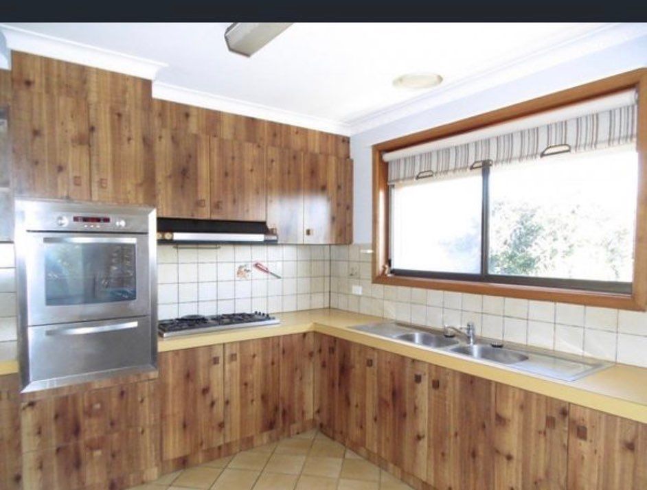 Kitchen with rustic wooden cabinets, stainless steel oven, gas stovetop, double sink under a large window, and beige countertops.