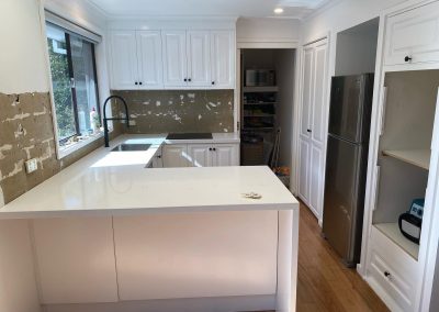 Partially renovated kitchen with white cabinets, stainless steel refrigerator, and unfinished backsplash.