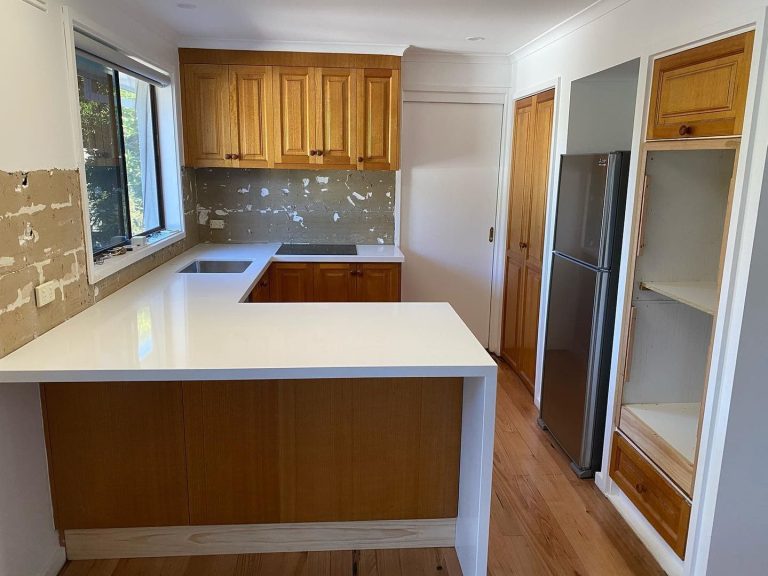 Kitchen under renovation with white countertops, wooden cabinets, and an unfinished backsplash.