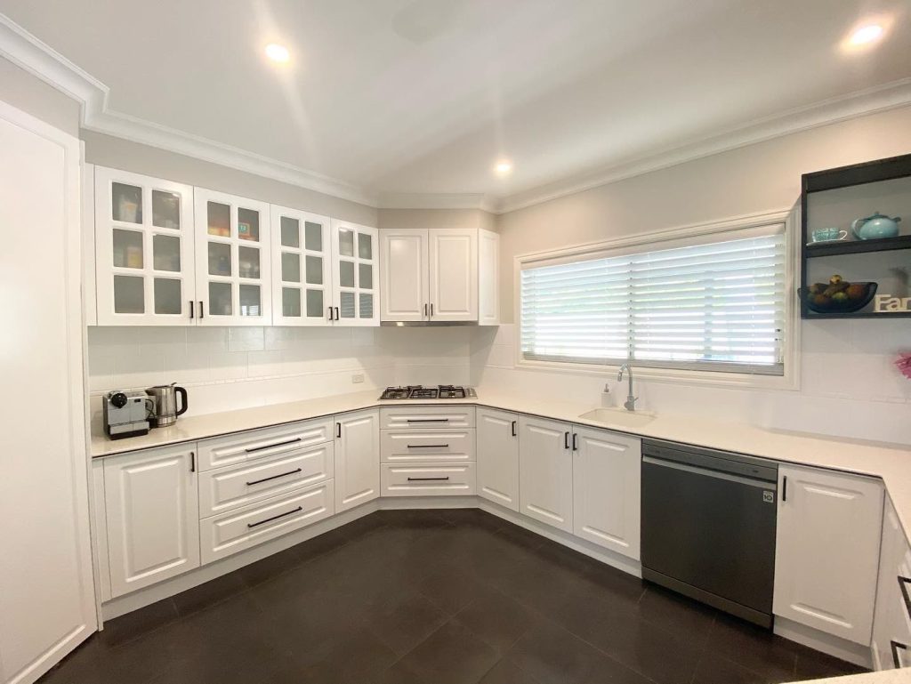 Modern white kitchen with glass-front cabinets, stainless steel appliances, gas stove, and dark tile flooring