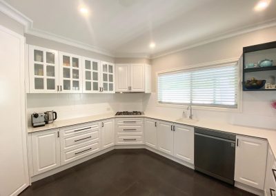 Modern white kitchen with glass-front cabinets, stainless steel appliances, gas stove, and dark tile flooring